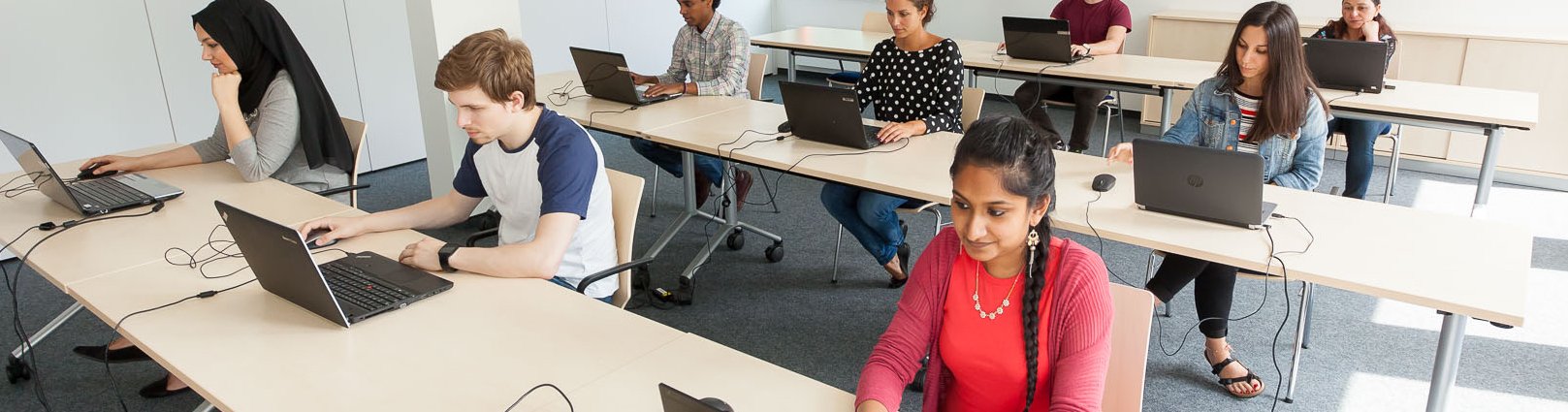 In einem Prüfungsraum legt eine Gruppe internationaler Studierender den C-Test an Laptops ab.  