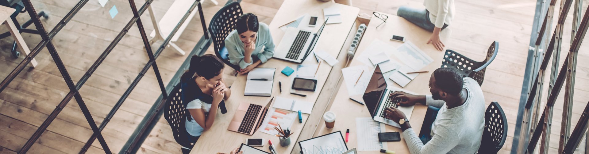 g.a.s.t.-Akademie: Fort- und Weiterbildung | iStock Das Imagebild illustriert die g.a.s.t.-Akademie. Es zeigt eine Gruppe junger Menschen, die zusammen an einem Tisch arbeiten. Auf dem Tisch stehen Laptops, Papier, Schreibmaterialien und Getränke sind auf der Arbeitsplatte verteilt.