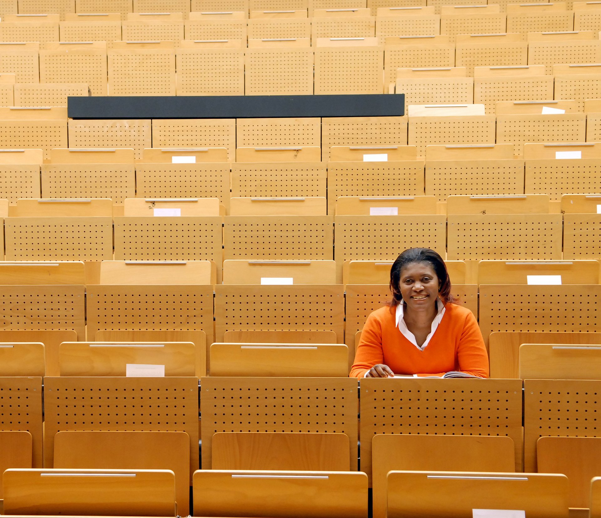 Eine farbige Studentin sitzt in einem leern Hörsaal und hat ihren Blick nach vorne gerichtet.