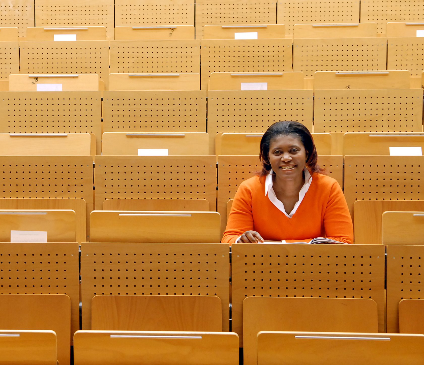 Eine farbige Studentin sitzt in einem leern Hörsaal und hat ihren Blick nach vorne gerichtet.