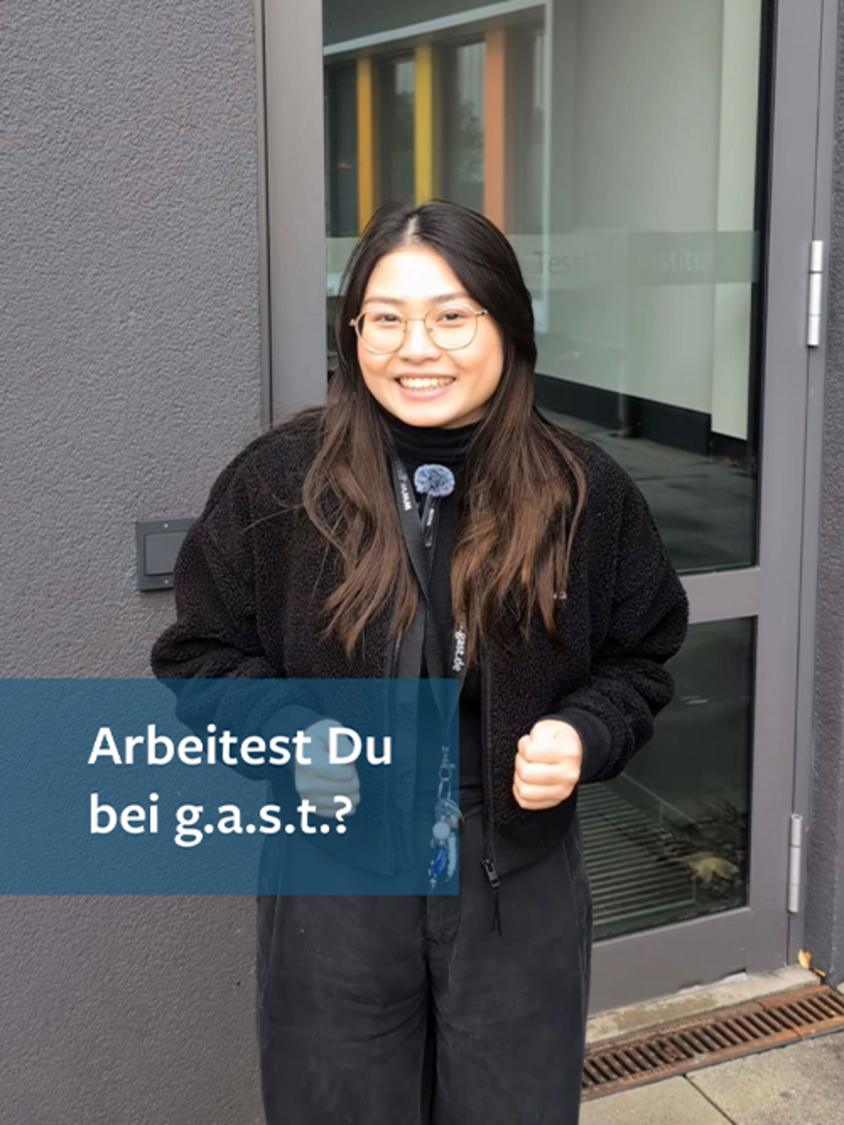 Eine junge Frau steht vor dem Gebäude der g.a.s.t. und fragt: Arbeitest Du bei g.a.s.t.?