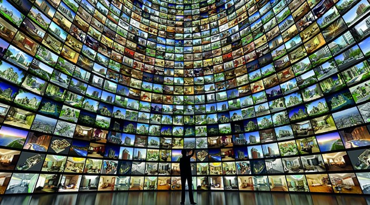 g.a.s.t.-Akademie | AdobeStock Vor einer hohen Wand aus leuchtenden Bildschirmen steht ein Mensch, der als Silhouette zu erkennen ist. Das Bild wird als Imagebild der g.a.s.t.-Akademie genutzt..