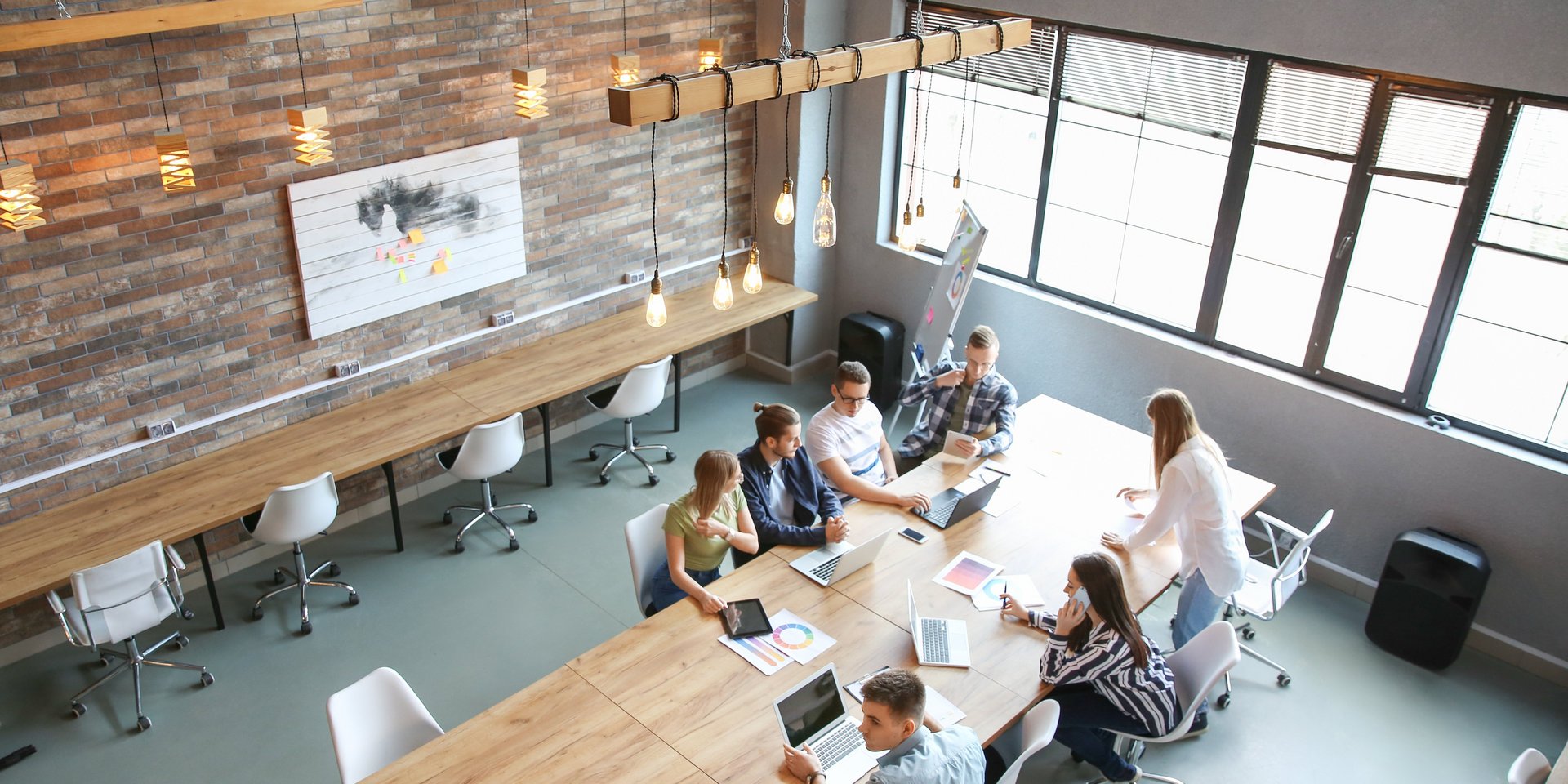 In einem Seminarraum mit Flipchart sitzen junge Menschen an einem Tisch vor ihren Laptops. Einige Papier liegen auf dem Tisch.